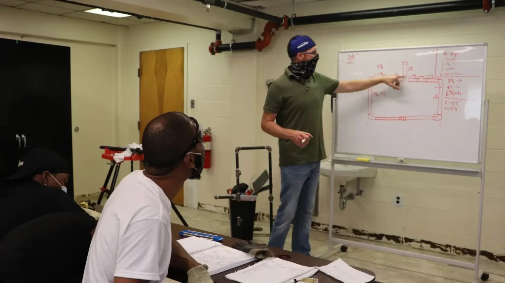 Pipefitting instructor explaining pipe layout during a classroom training session.