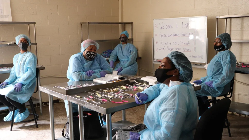  A surgical technologist in full sterile gown and gloves organizing instruments on a back table in an operating room. 