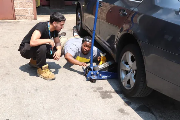 Students receiving hands-on automotive training while inspecting a raised vehicle.